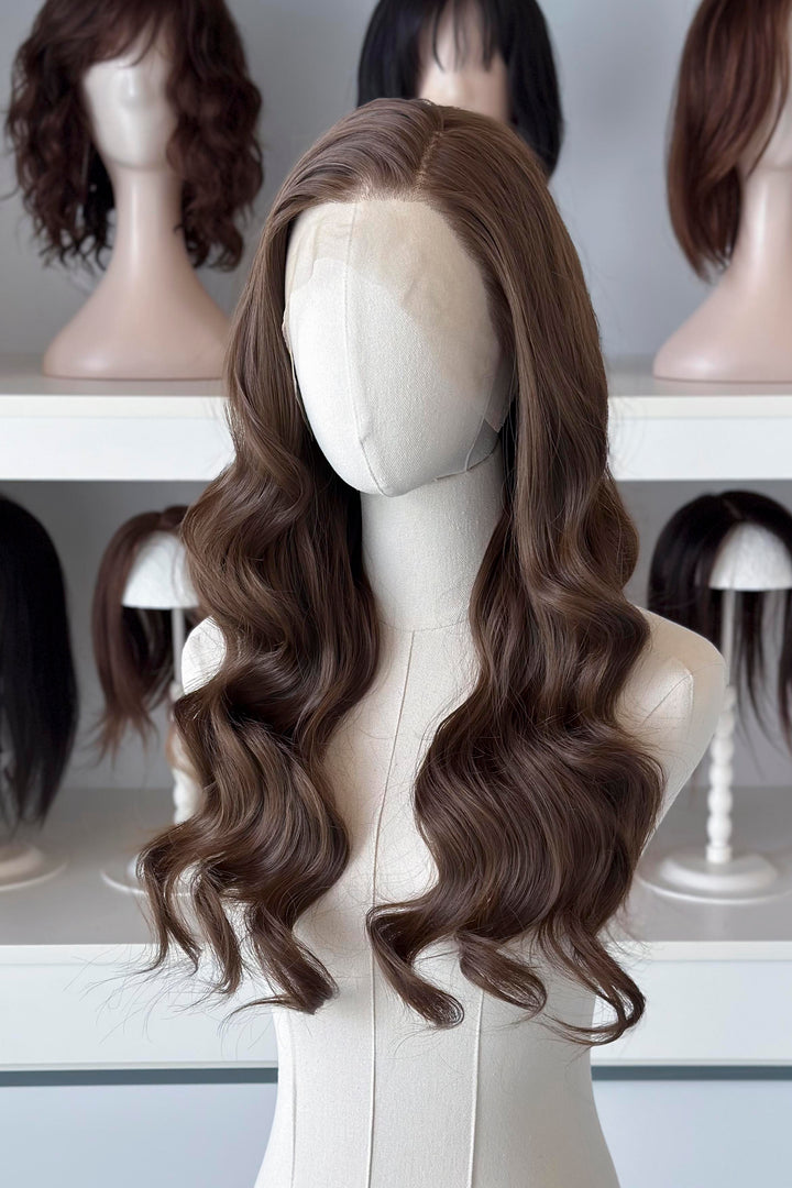 Brown wig on a mannequin head with blurred wigs in the background
