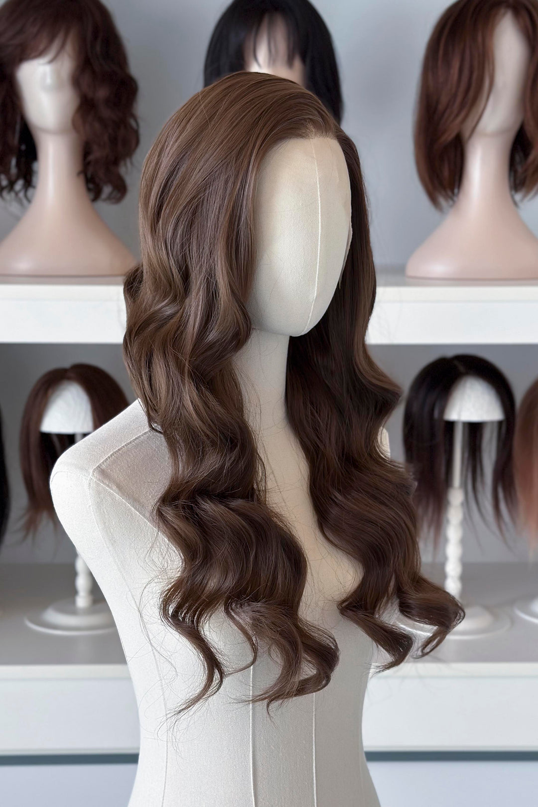 Brown wig on a mannequin head with blurred wigs in the background