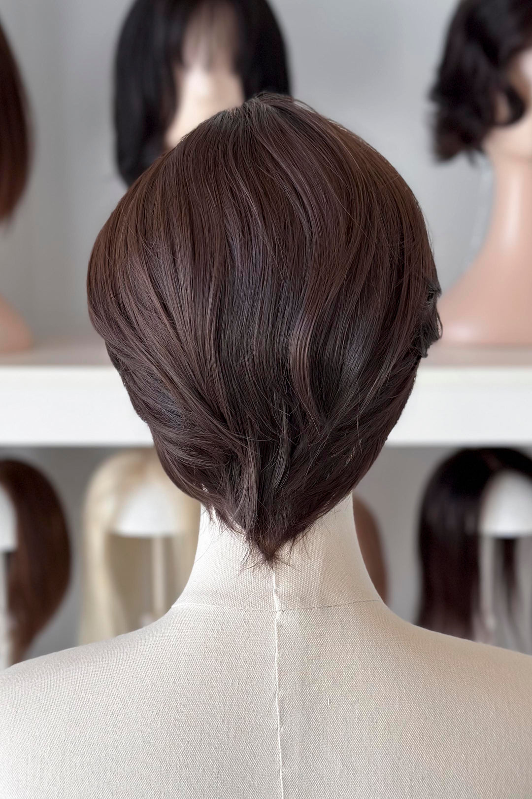 Brown short wig on a mannequin head with blurred wigs in the background
