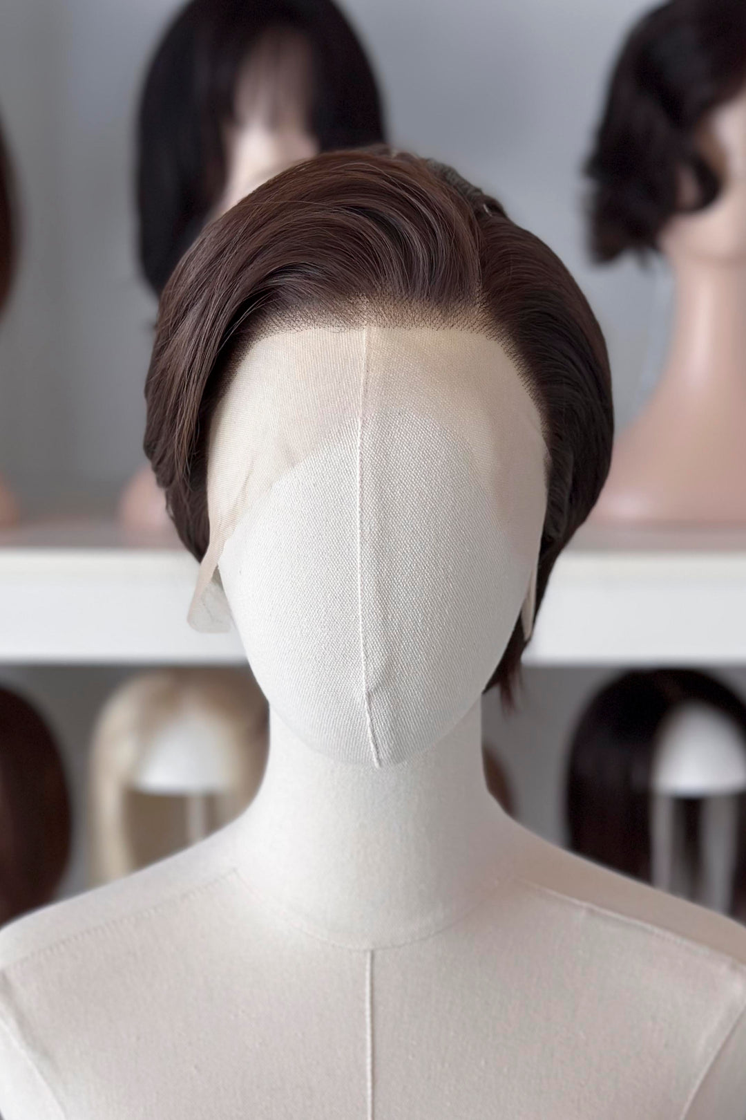 Brown short wig on a mannequin head with blurred wigs in the background