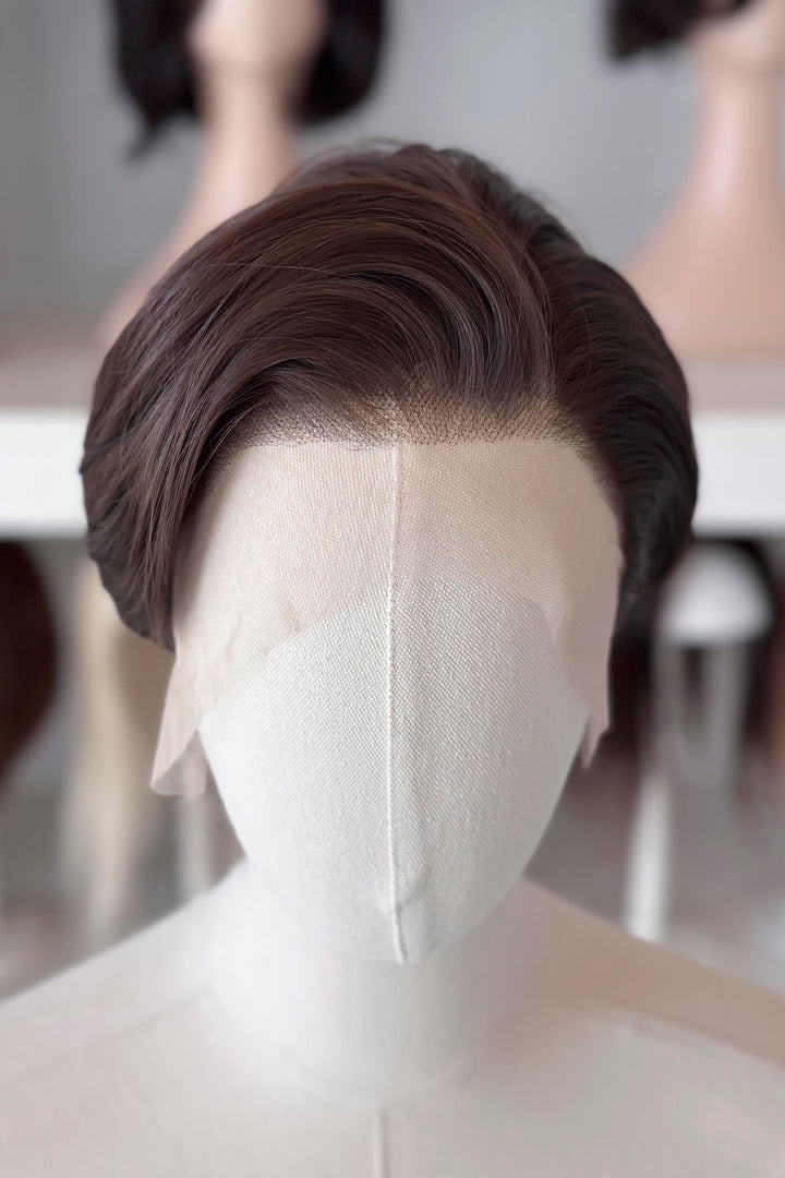 Brown short wig on a mannequin head with blurred wigs in the background