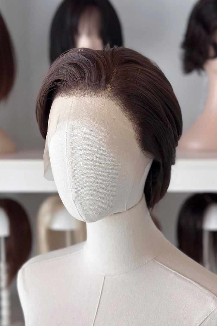 Brown short wig on a mannequin head with blurred wigs in the background