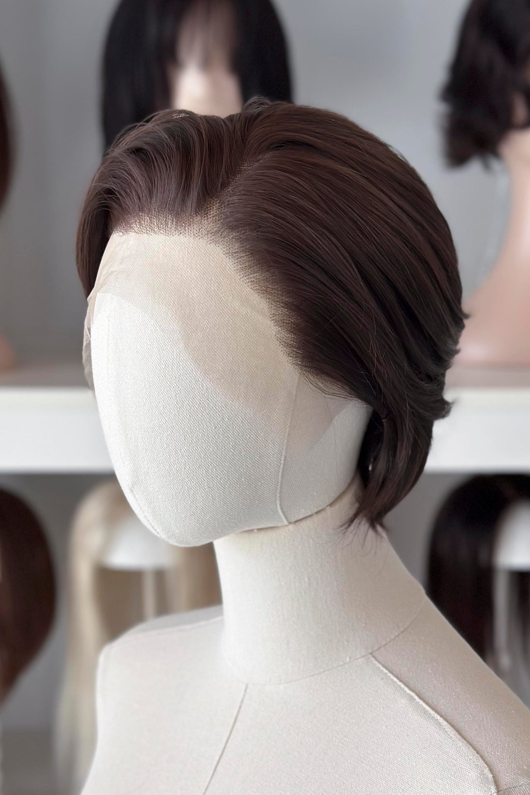 Brown short wig on a mannequin head with blurred wigs in the background