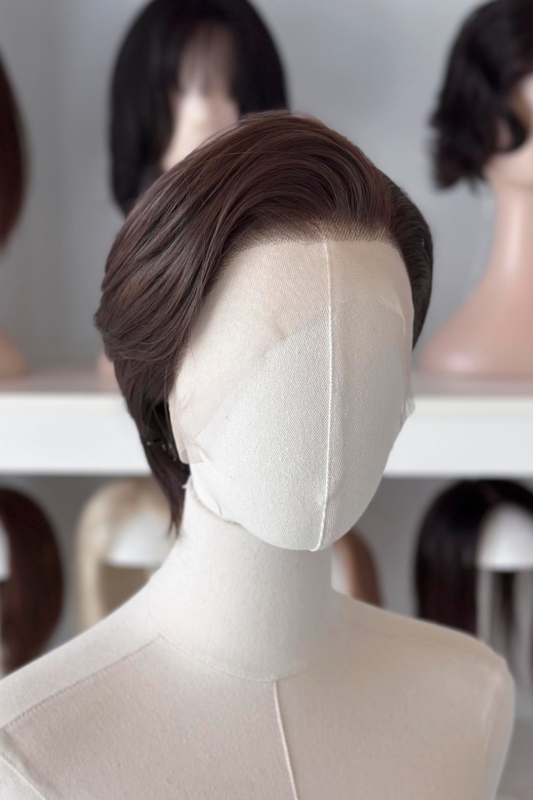 Brown short wig on a mannequin head with blurred wigs in the background