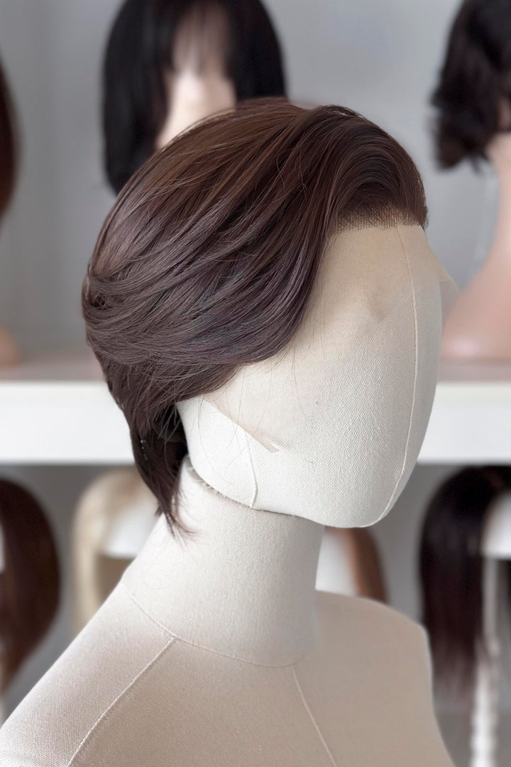 Brown short wig on a mannequin head with blurred wigs in the background