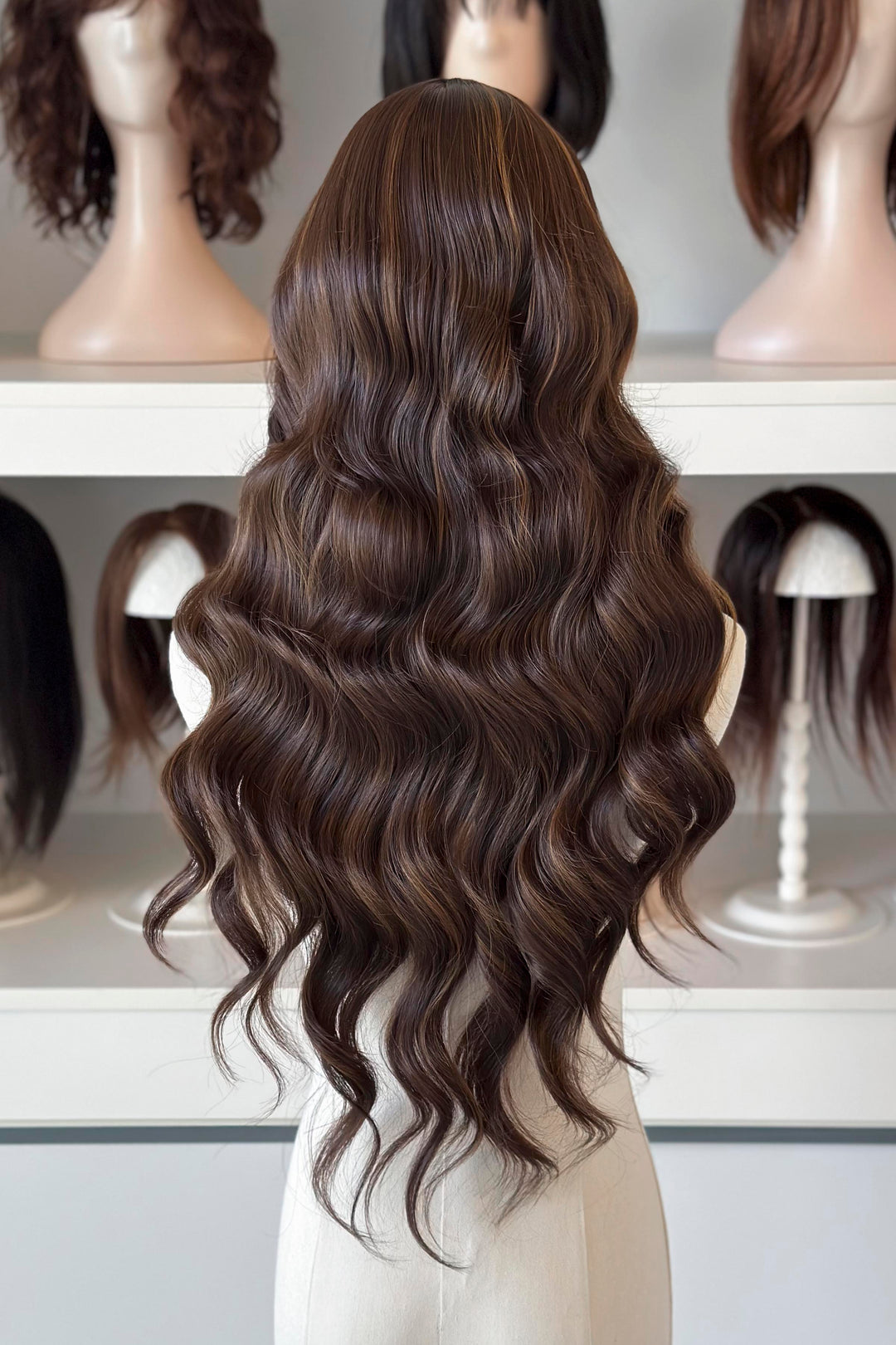 Brown wig with blonde highlights on a mannequin head with blurred wigs in the background