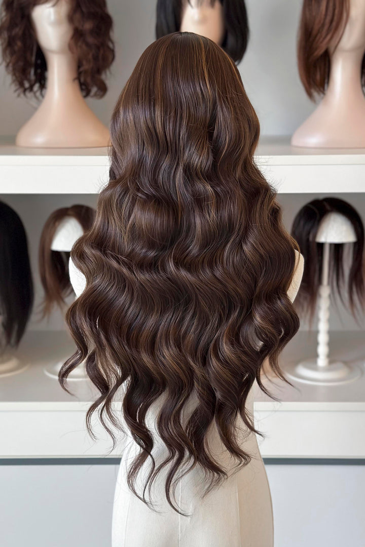 Brown wig with blonde highlights on a mannequin head with blurred wigs in the background