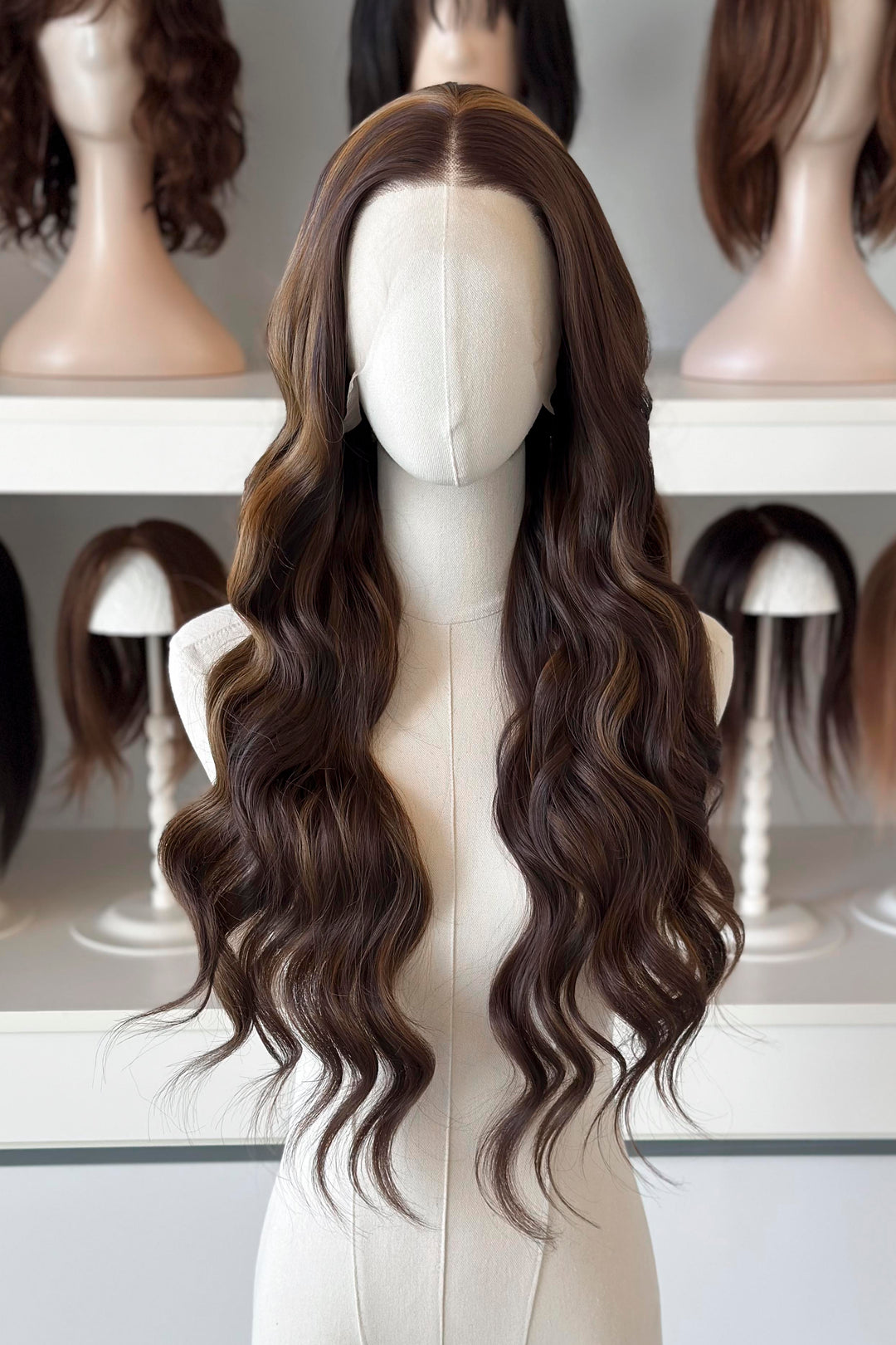 Brown wig with blonde highlights on a mannequin head with blurred wigs in the background
