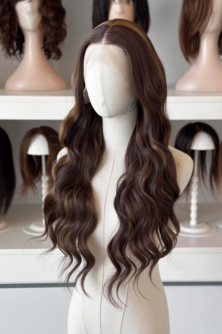 Brown wig with blonde highlights on a mannequin head with blurred wigs in the background