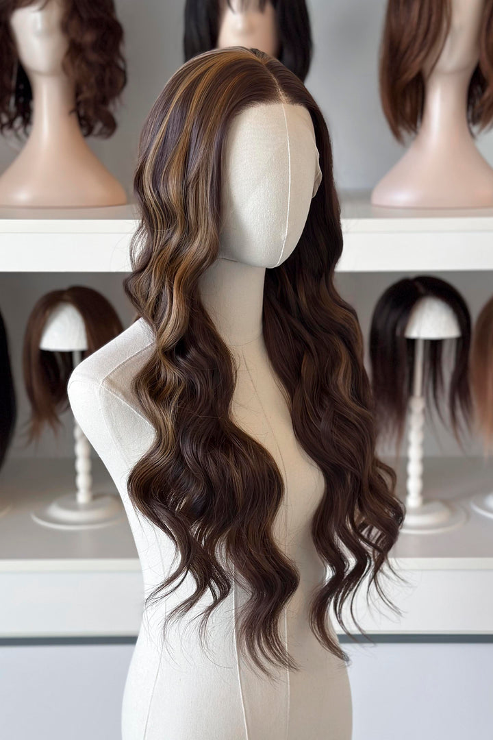 Brown wig with blonde highlights on a mannequin head with blurred wigs in the background