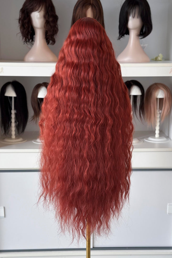 Extra-long red wig on a mannequin head with other wigs in the background