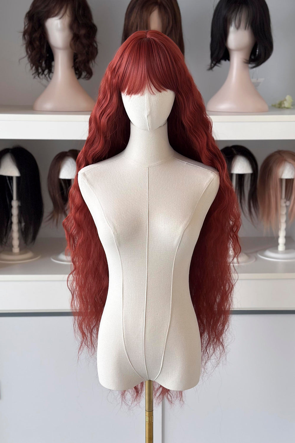 Extra-long red wig on a mannequin head with other wigs in the background