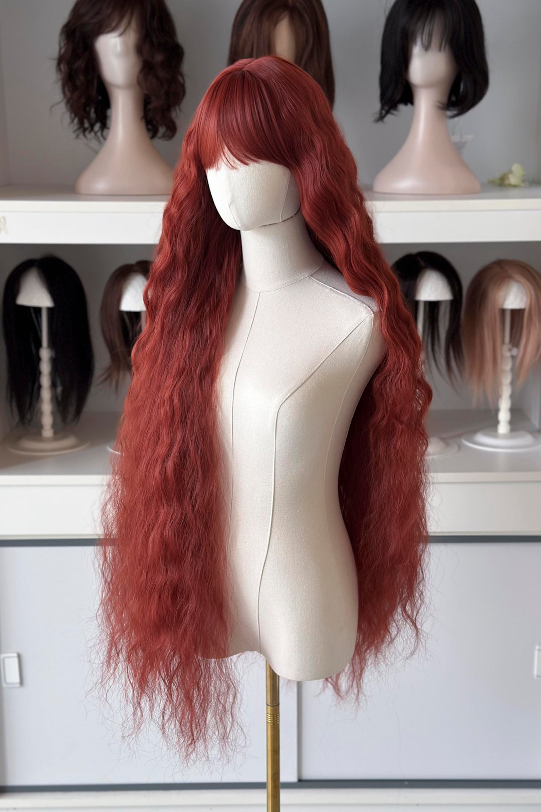Extra-long red wig on a mannequin head with other wigs in the background