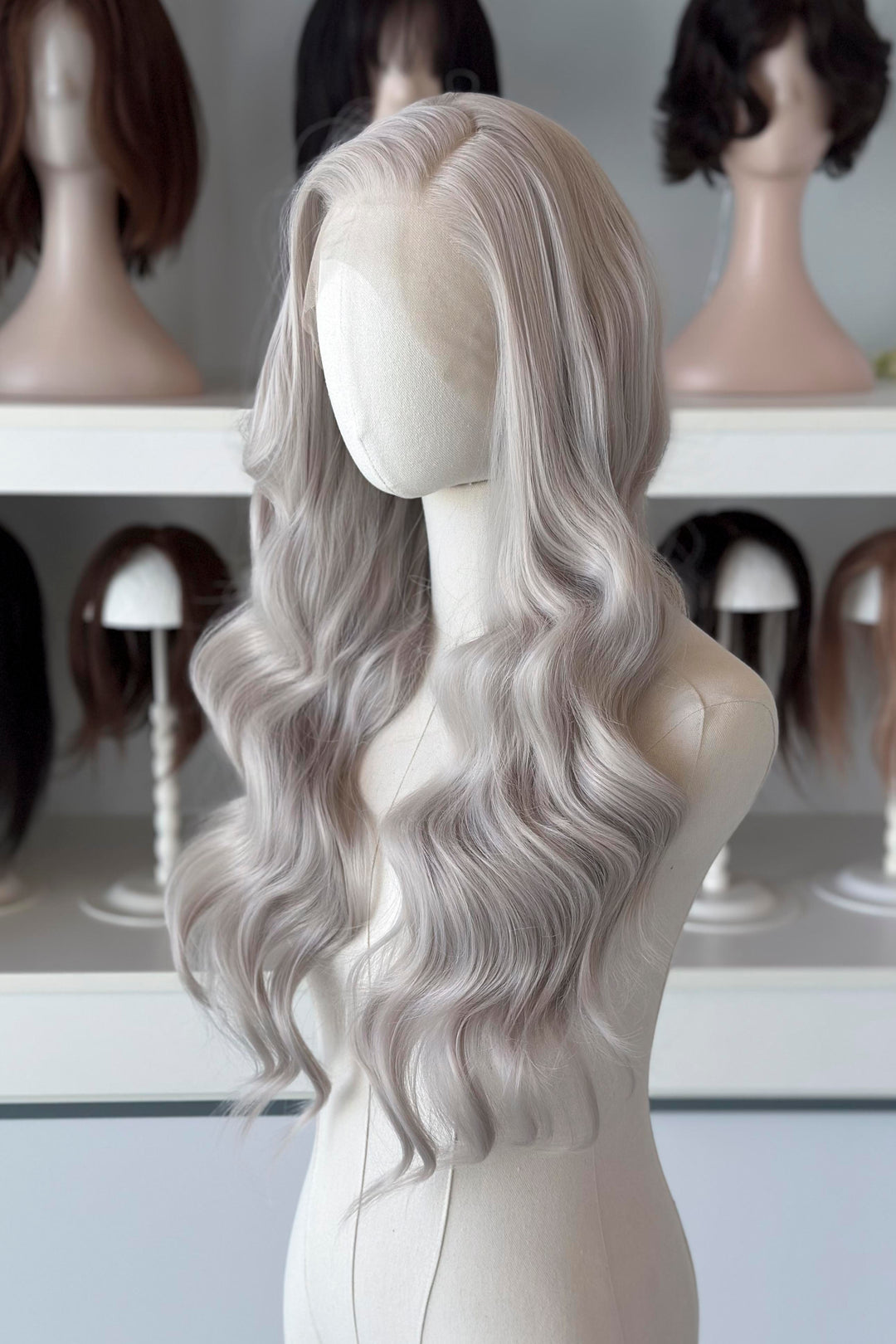 Silver lace front wig on a mannequin head with blurred wig display in the background