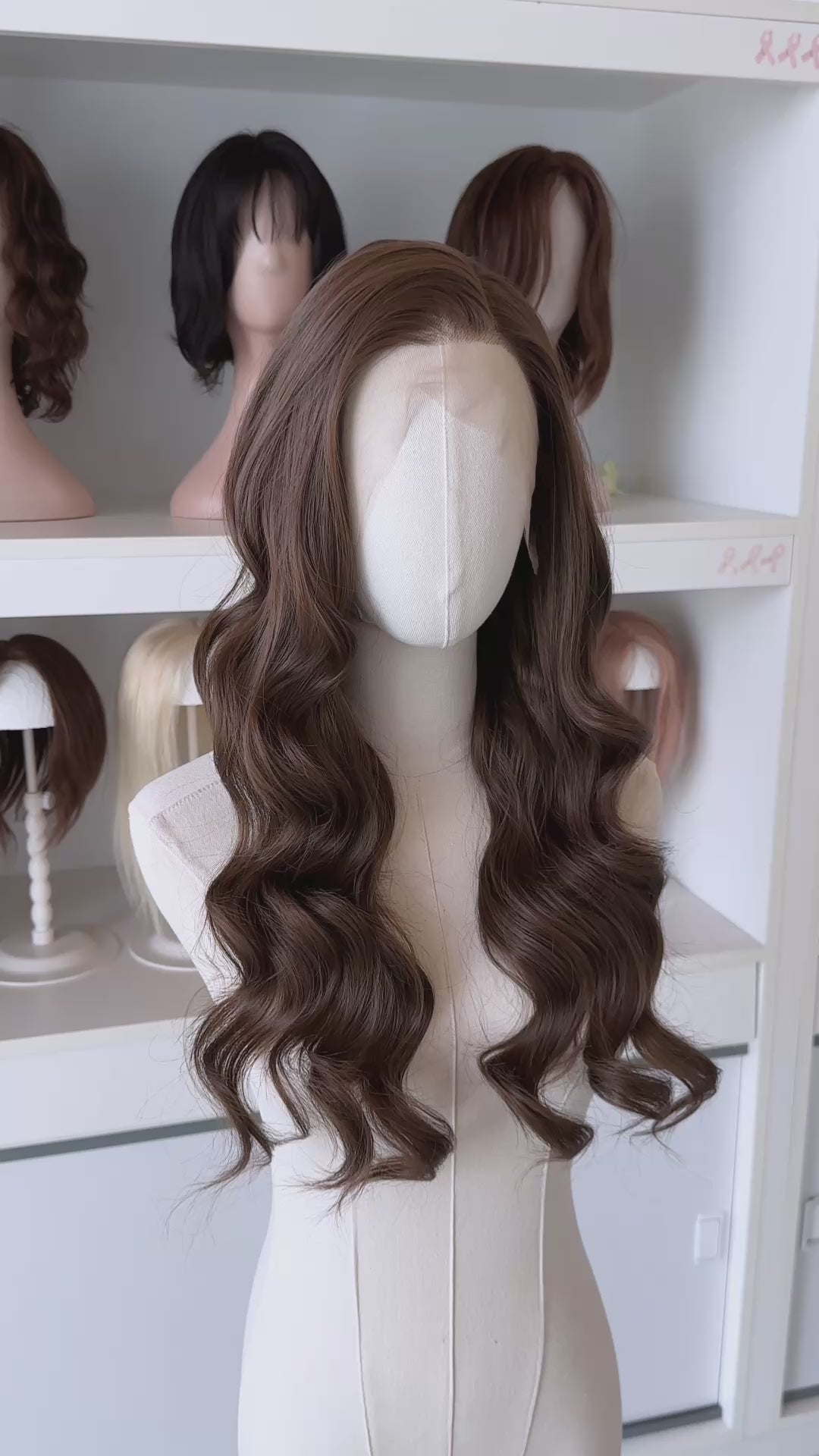 Brown wig on a mannequin head with blurred wigs in the background