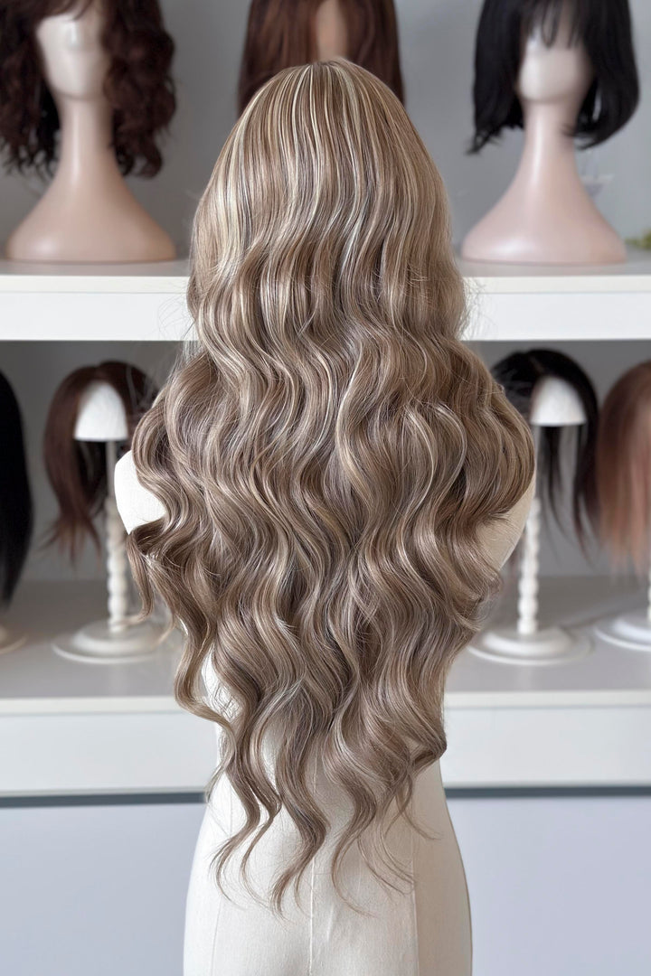 Ash brown hair with chunky blonde highlights wig on a mannequin head with blurred wigs in the background
