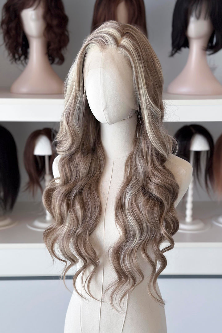 Ash brown hair with chunky blonde highlights wig on a mannequin head with blurred wigs in the background