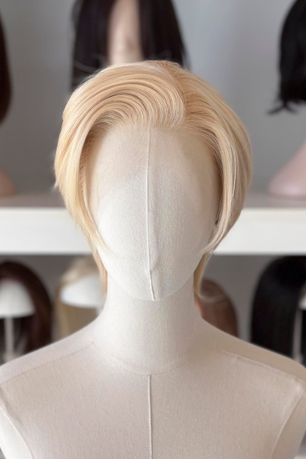 Blonde Short Lace wig on a mannequin head with blurred wig display in the background