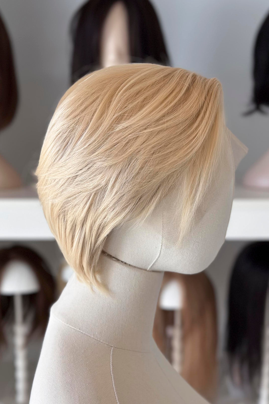 Blonde Short Lace wig on a mannequin head with blurred wig display in the background