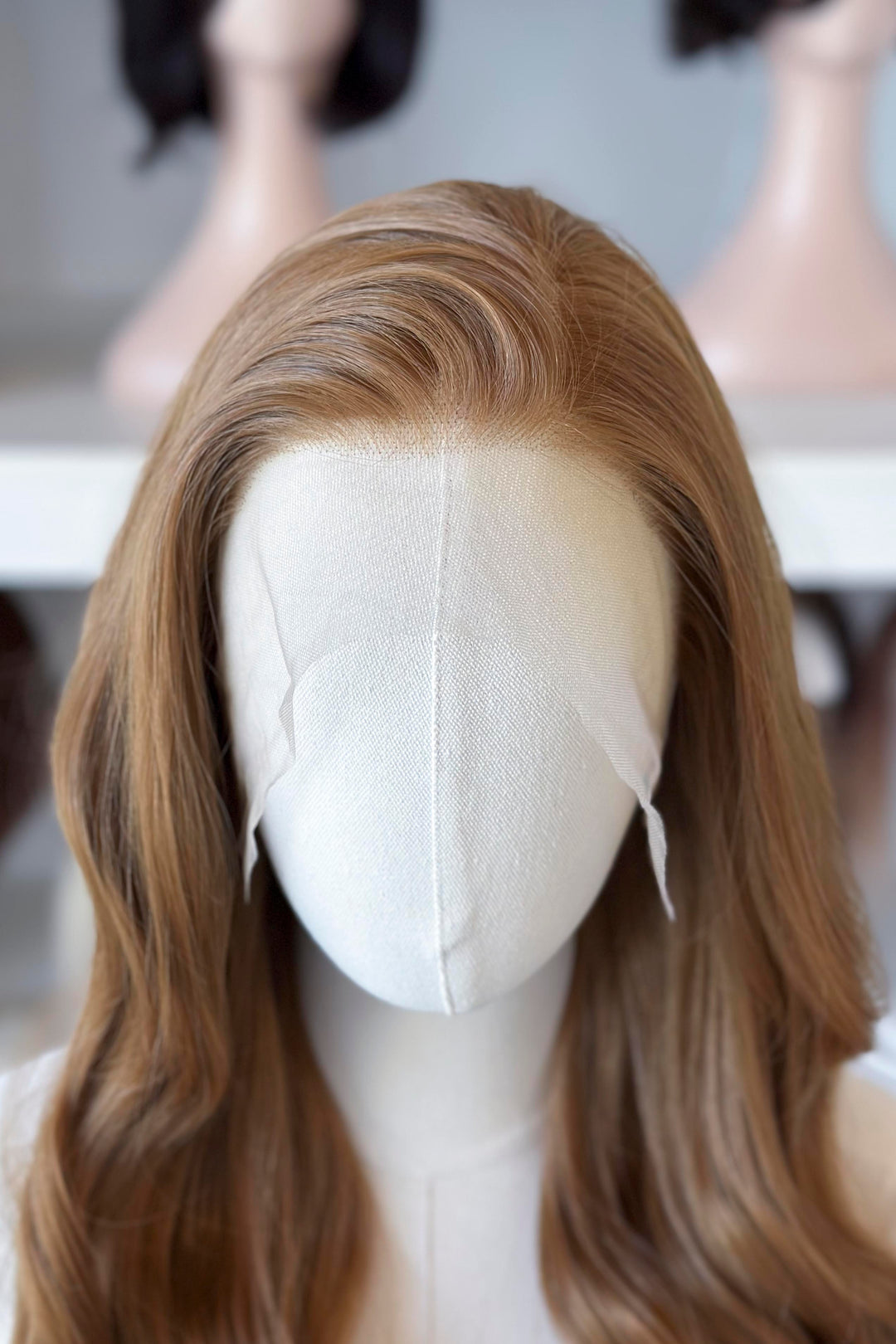  a long, wavy copper brown blonde wig in a wig store setting.