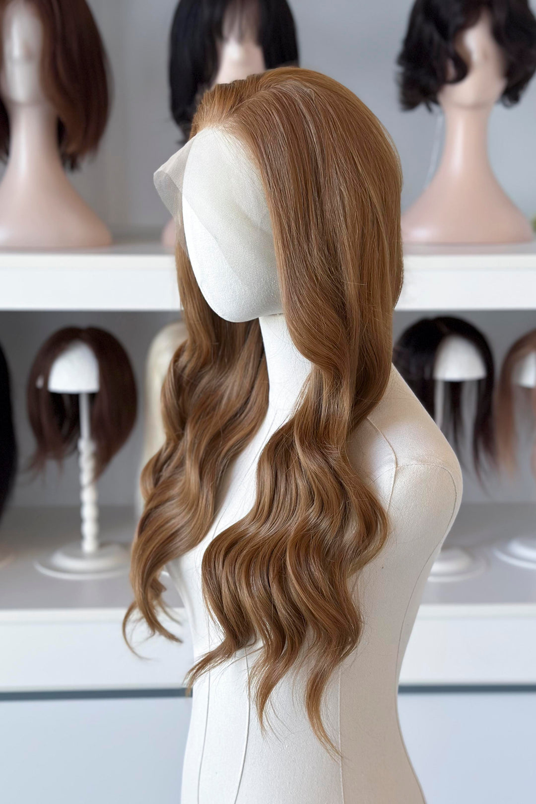  a long, wavy copper brown blonde wig in a wig store setting.