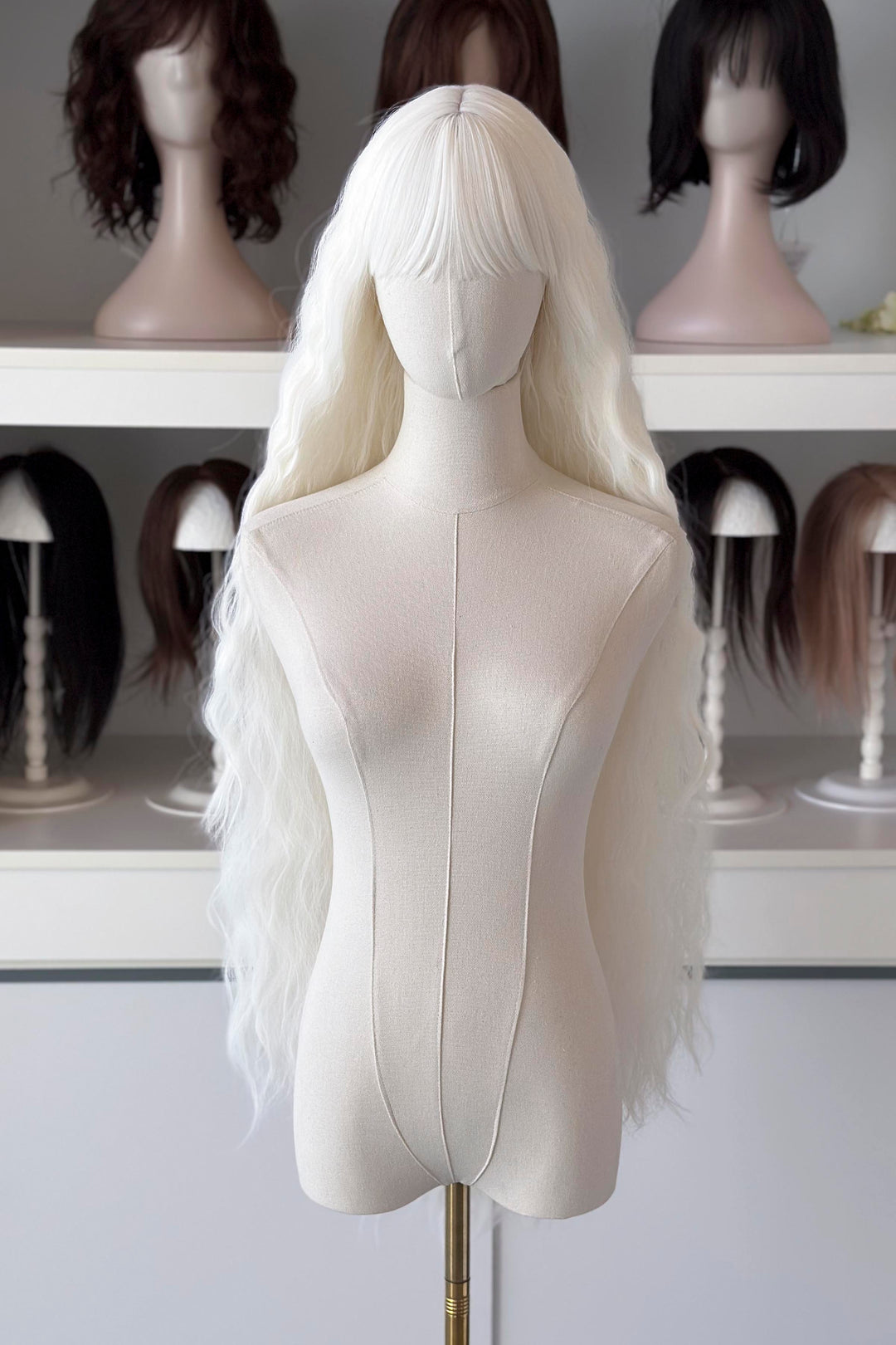 long white wig in front of other mannequin heads with wigs on a shelf.