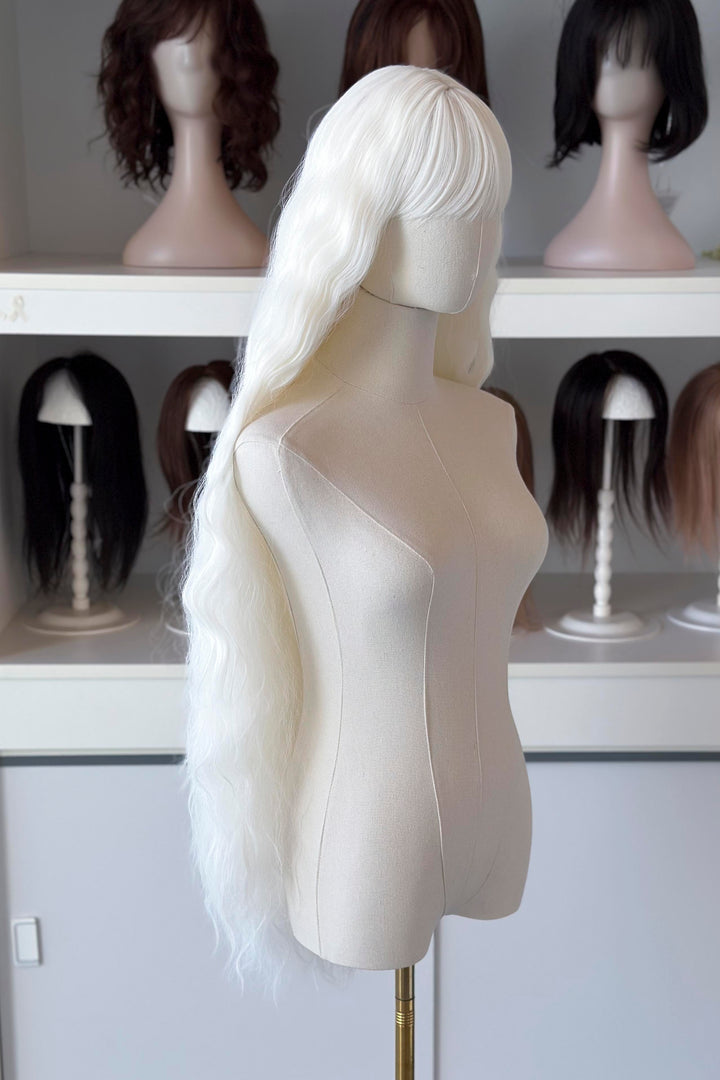 long white wig in front of other mannequin heads with wigs on a shelf.
