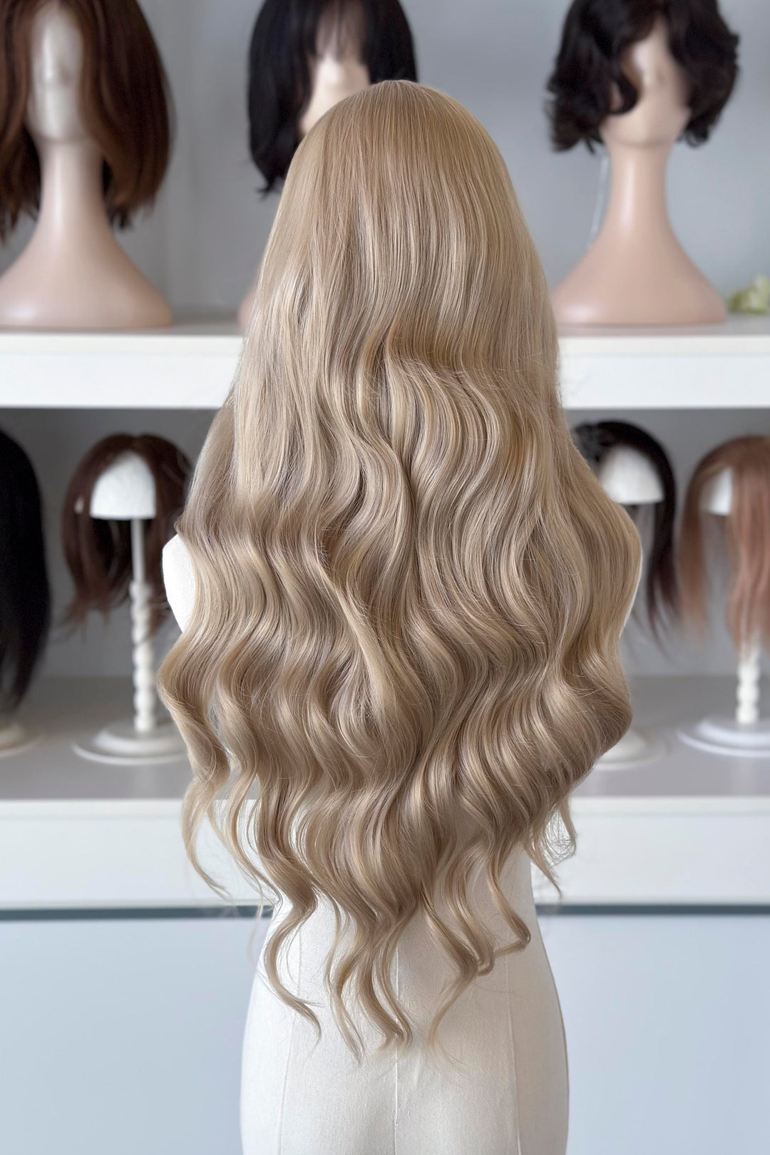 Light Golden Blonde wig on a mannequin head with blurred wig mannequins in the background, good for Aelin Galathynius cosplay