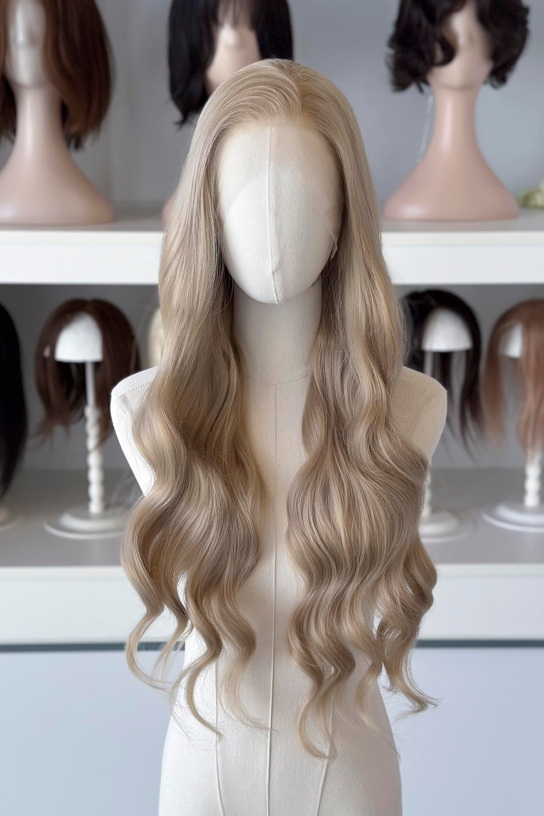 Light Golden Blonde wig on a mannequin head with blurred wig mannequins in the background, good for Aelin Galathynius cosplay