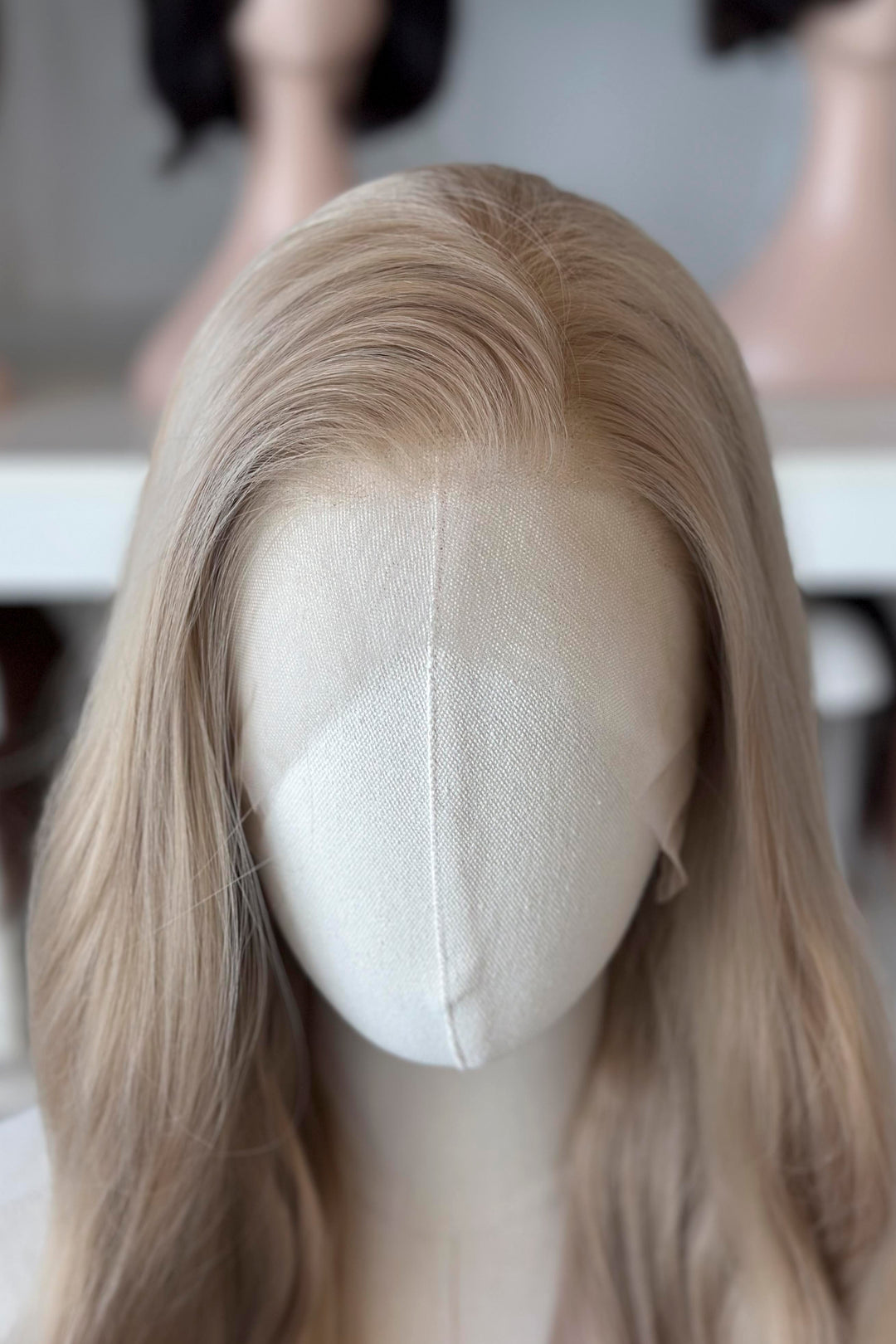 Light Golden Blonde wig on a mannequin head with blurred wig mannequins in the background, good for Aelin Galathynius cosplay