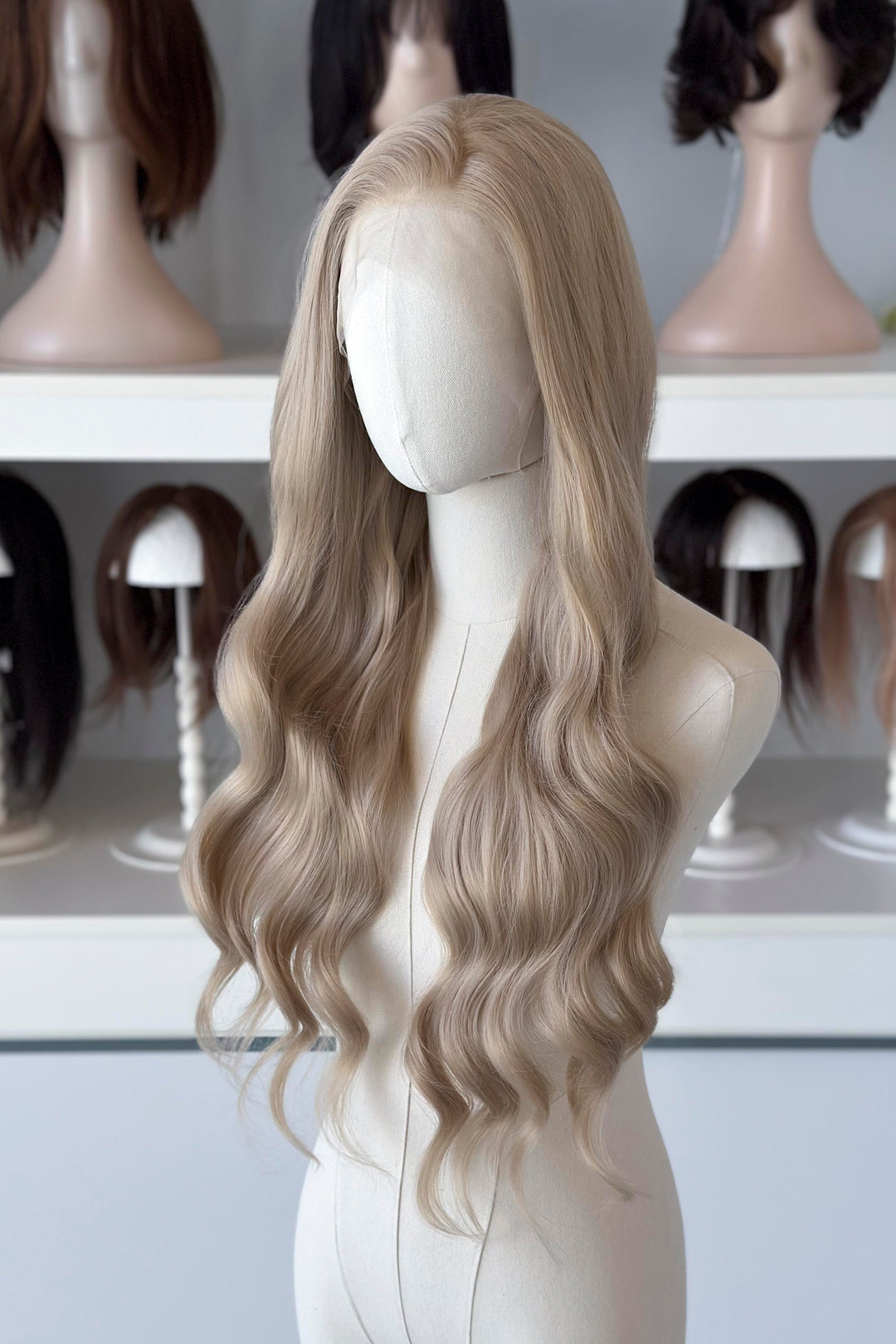 Light Golden Blonde wig on a mannequin head with blurred wig mannequins in the background, good for Aelin Galathynius cosplay