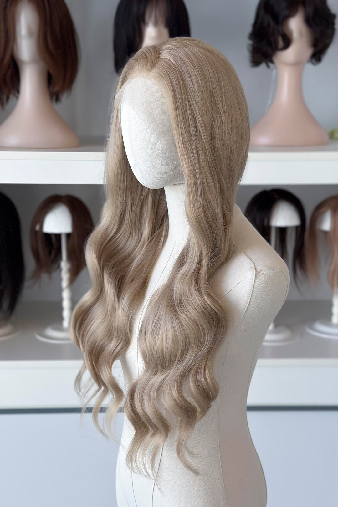 Light Golden Blonde wig on a mannequin head with blurred wig mannequins in the background, good for Aelin Galathynius cosplay