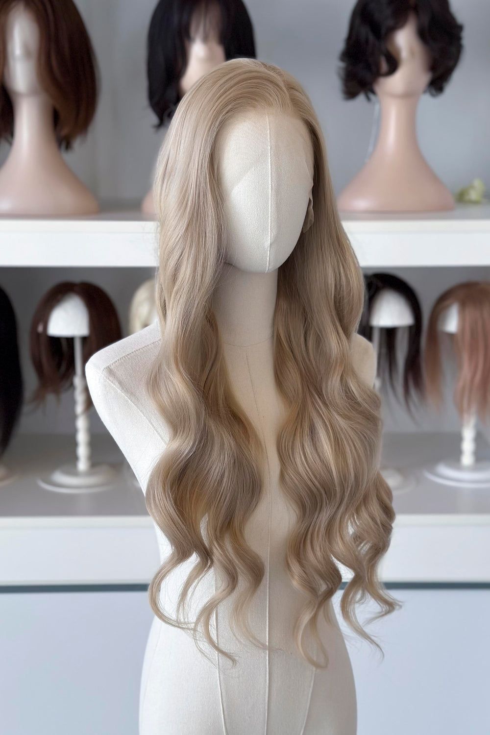 Light Golden Blonde wig on a mannequin head with blurred wig mannequins in the background, good for Aelin Galathynius cosplay